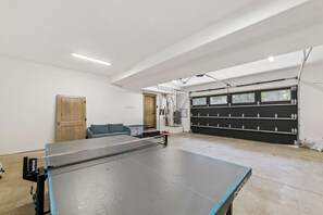 A spacious indoor area with a ping pong table, a couch, and a garage door.