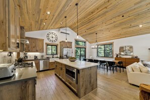 A spacious kitchen with wooden cabinets, a central island, and a dining area with a view of the outdoors. - The Pine & Trail Tahoe | 4BR | Hot Tub + 3 Kings (South Lake Tahoe)