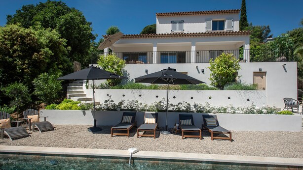 A poolside area with lounge chairs and umbrellas, a clear pool, and a house with a tiled roof and white walls. - Luxury villa with A/C and a heated private pool (La Croix-Valmer)