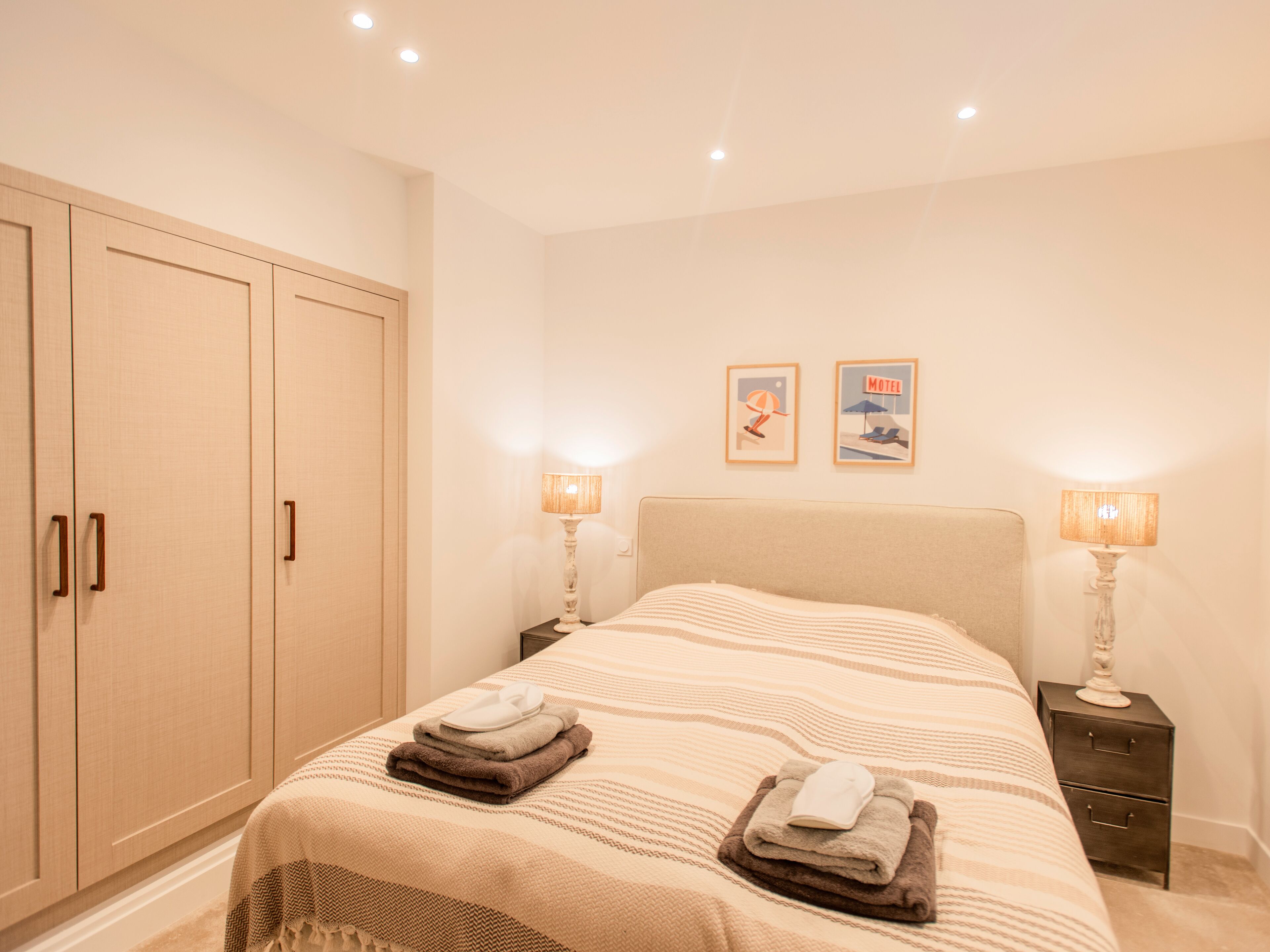 Un dormitorio con cama, dos mesitas de noche, un armario y dos cuadros colgados en la pared.