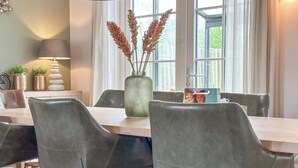 Un coin repas avec une table en bois, des chaises à revêtement gris, un vase contenant des plantes séchées et une lampe.