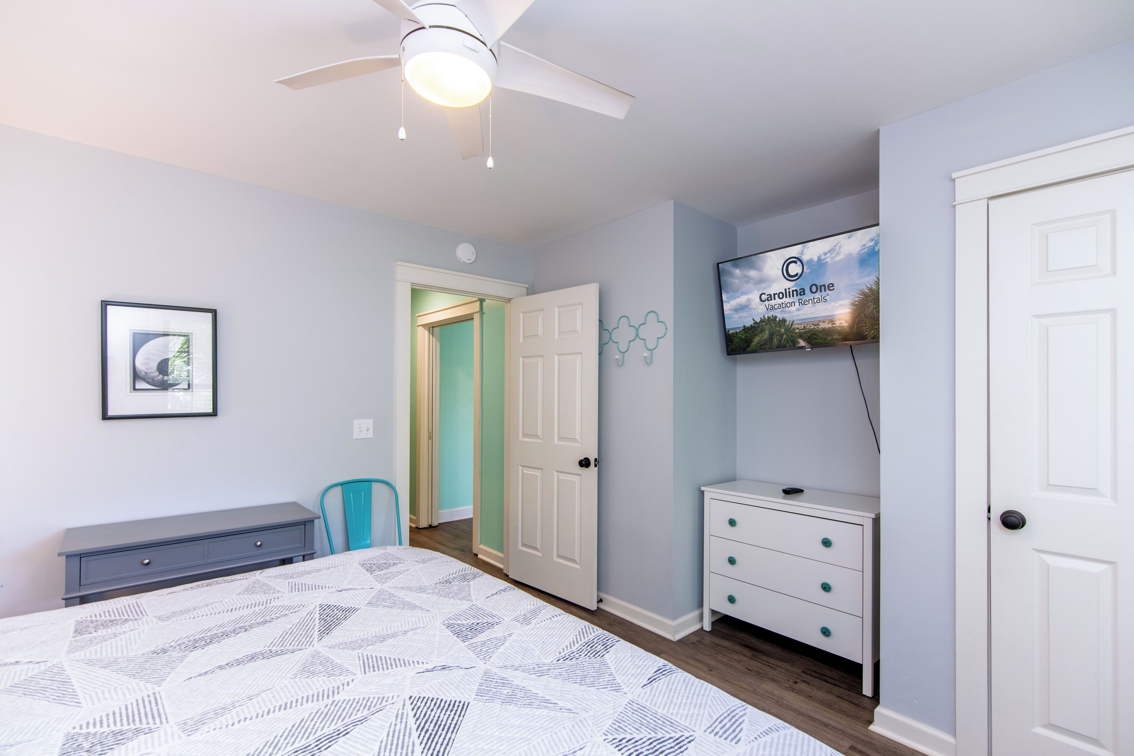 Une chambre à coucher avec un lit, un ventilateur de plafond, une télévision, une porte et un petit bureau.