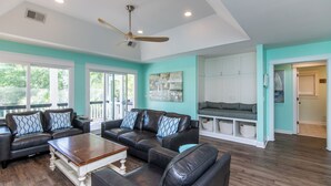 A spacious living room with a large black leather sofa set, a wooden coffee table, and a ceiling fan. - Knot in Kansas; Pet-Friendly, Sleeps 10, 1 Block to Beach, Firepit & Ping-Pong (Edisto Beach)