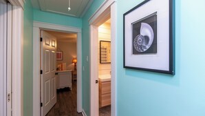 A hallway with a light blue wall, a framed artwork, and a door leading to a bathroom. - Knot in Kansas; Pet-Friendly, Sleeps 10, 1 Block to Beach, Firepit & Ping-Pong (Edisto Beach)