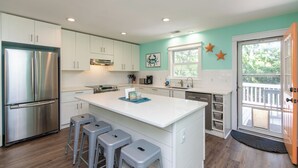 A modern kitchen with white cabinets, stainless steel appliances, and a teal accent wall. - Knot in Kansas; Pet-Friendly, Sleeps 10, 1 Block to Beach, Firepit & Ping-Pong (Edisto Beach)