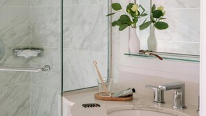 Une salle de bain avec un mur en marbre, une douche en verre, un lavabo blanc doté d’un robinet moderne et un miroir au-dessus du lavabo.