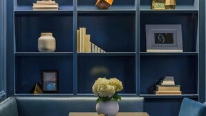 Une pièce avec un canapé bleu, une table sur laquelle se trouvent un vase et des fruits, et une bibliothèque remplie de divers objets.