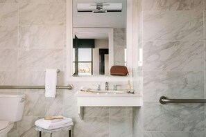 A bathroom with a white sink, mirror, and marble tiles. - No. 284 Powered by Sonder (Boston)