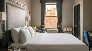 Une chambre d’hôtel avec un grand lit, un bureau, une chaise, une fenêtre avec des rideaux et une vue sur un bâtiment à l’extérieur.
