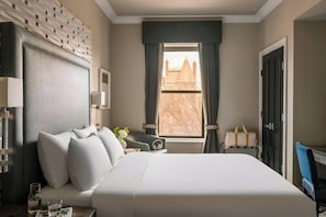 Habitación de hotel con una cama grande, un escritorio, una silla, una ventana con cortinas y vista a un edificio.