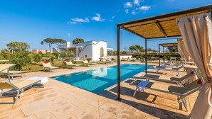A swimming pool with lounge chairs, a covered seating area, and a white building in the background. - Villa Elysium for 10 With Pool Near Gallipoli (Alezio)
