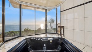 Ein modernes Badezimmer mit einer großen Badewanne, Meerblick und einem kleinen Holzschemel.