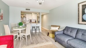 A modern living room with a grey sofa, a red chair, a dining area with a table and chairs, and a kitchen in the background. - Oceanfront Condo in Harbor Island Community! (St Helena Island)
