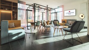 A modern hotel lobby with a seating area, a coffee table, and a large window with curtains.