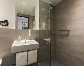 A modern bathroom with a glass shower enclosure, a white sink with a mirror, and a towel rack. - Candlewood Suites BERLIN CHARLOTTENBURG by IHG (Berlin)