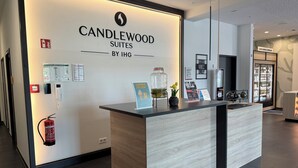 A reception desk with a sign for Candlewood Suites by IHG, a fire extinguisher, a phone, and a small potted plant. - Candlewood Suites BERLIN CHARLOTTENBURG by IHG (Berlin)