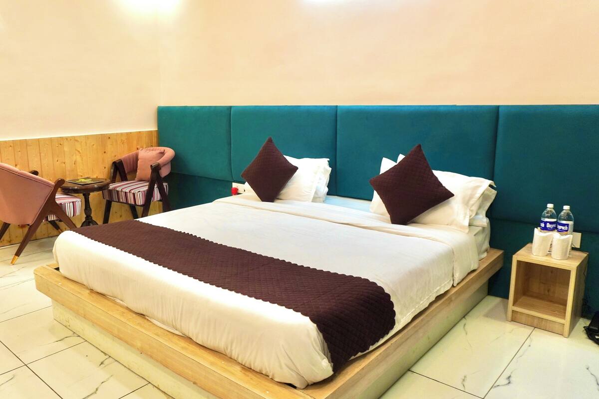 A hotel room with a large bed, a wooden headboard, a small table with chairs, and a wooden nightstand with water bottles.