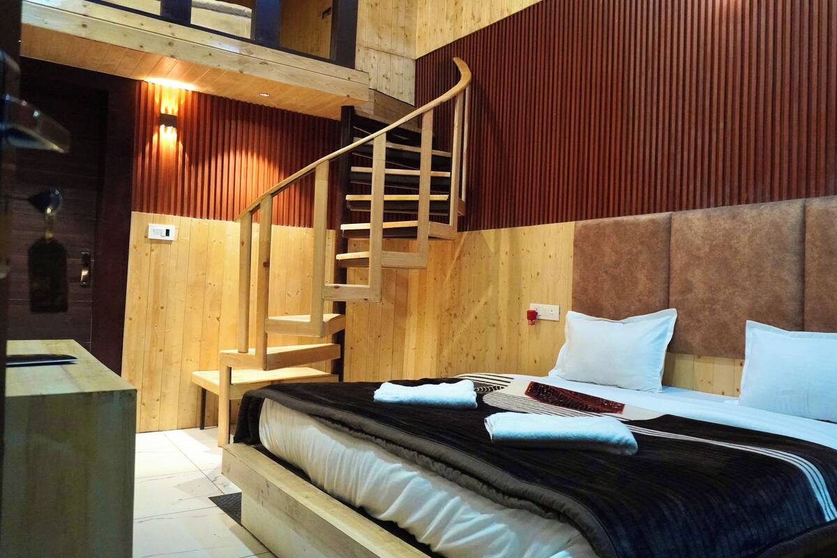 A wooden room with a bed, a staircase, and a red wall.