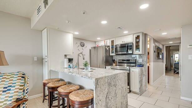 A modern kitchen with a large island, stainless steel appliances, and a dining area with bar stools. - Pool Access: Beachfront Condo in Cape Canaveral! (Cape Canaveral)