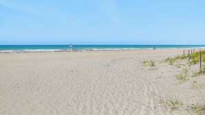 A wide sandy beach with gentle waves, a lifeguard tower, and a distant pier. - Pool Access: Beachfront Condo in Cape Canaveral! (Cape Canaveral)