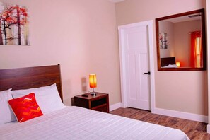A hotel room with a bed, a nightstand with a lamp, a door, and a mirror on the wall.
