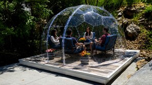 Una estructura de cúpula transparente con asientos en su interior, rodeada de follaje.
