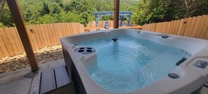 A hot tub on an outdoor deck with a wooden fence and a view of a wooden pergola.
