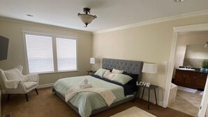 Une chambre à coucher avec un grand lit, une chaise, un bureau et une salle de bain visible à travers une porte ouverte.