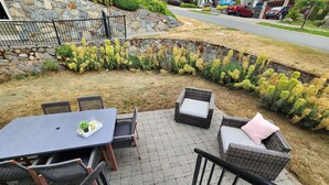 Un espace extérieur aménagé en terrasse, avec une table et des chaises, un mur en pierre et une vue sur la rue.