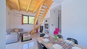 Un interior moderno con una escalera de madera, un sofá, una mesa de comedor para cuatro personas y una chimenea.