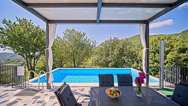 Un espacio al aire libre cubierto con piscina, sillas y una mesa con frutero.