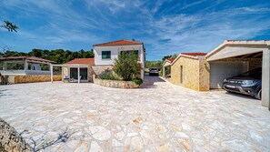 A stone-paved driveway leading to a house with a garage and a covered patio area.