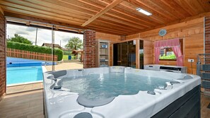 Una banyera d'hidromassatge en una cabana de fusta amb una piscina a l'exterior.