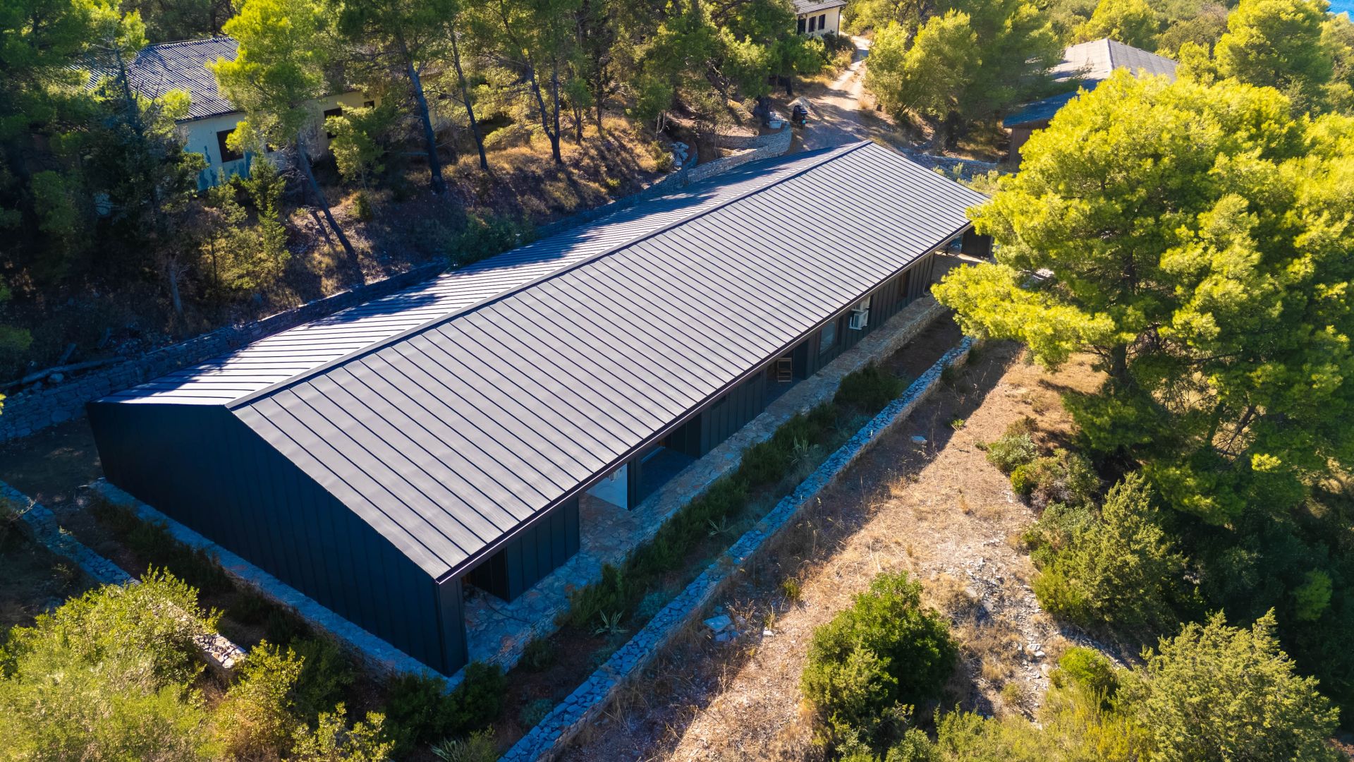 A long, narrow building with a dark roof, surrounded by trees and a stone pathway.