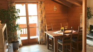 Ein Holzinterieur mit einem Esstisch, Stühlen, einer Zimmerpflanze und einer Wanduhr.