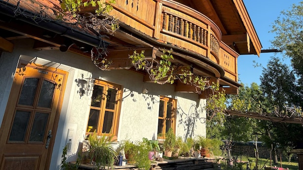 Ein traditionelles Holzhaus mit Balkon, großen Fenstern und einer Steinmauer im Hintergrund.