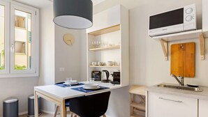 A compact kitchen with a microwave, shelves with glassware, a sink, and a dining area with chairs. - GuestHost - Simplon & Garibaldi Comfy Studio (Milano)