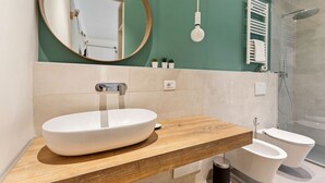 A modern bathroom with a round mirror, a vessel sink, a wooden vanity, a toilet, and a shower area. - GuestHost - Simplon & Garibaldi Comfy Studio (Milano)