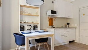 A compact kitchen with white cabinets, a microwave, and a dining area with a table and chairs. - GuestHost - Simplon & Garibaldi Comfy Studio (Milano)