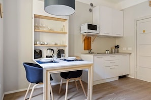 A compact kitchen with white cabinets, a microwave, and a dining area with a table and chairs.