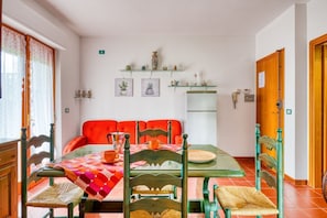 Zona pranzo con tavolo apparecchiato per quattro, circondato da sedie, un frigorifero e mensole con oggetti decorativi.