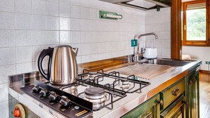 A kitchen with a gas stove, kettle, and stainless steel sink.