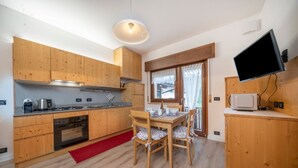 Een moderne keuken met houten kastjes, een eettafel met stoelen, een rood vloerkleed en een televisie aan de muur.