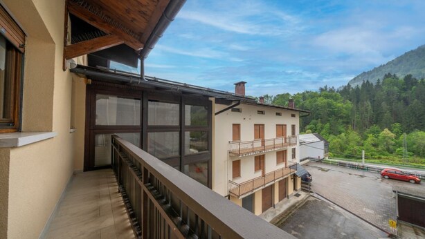 Een balkon met uitzicht op een gebouw en een bebost berglandschap.