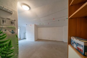 A room with a white wall, a ceiling light, a power outlet, and a shelf with a box.