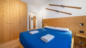 Een slaapkamer met een houten hoofdbord, een bed met blauw beddengoed, twee opgerolde handdoeken en houten ski's aan de muur.