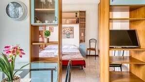 A room with a bed, a desk with a chair, a TV, and shelves with various items. - GuestHost - Comfortable apartment equipped with all comforts to accommodate up to 3 people, located a stone's throw from Fontivegge Station (80 meters) and a 5-minute walk from Pescaia Park. It is located in a quiet residential area well equipped with al (Perugia)