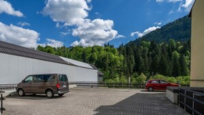 A paved parking area with a building and a mountain in the background. - GuestHost - Cozy Apartment X3 in Tarvisio Center (Tarvisio)
