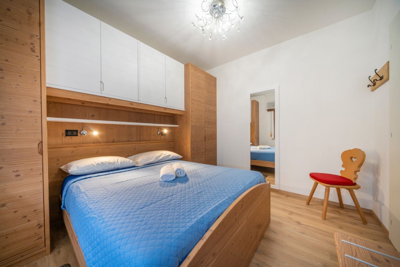 A bedroom with a bed, wooden wardrobe, and a chair.