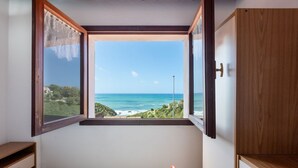 A bedroom with a view of the sea, a wooden wardrobe, and a bed with a striped bedspread. - GuestHost - Sea's Peace (Torre dei Corsari)